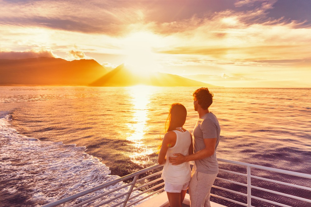 A couple enjoying a romantic sunset on a boat, against the colorful evening sky.